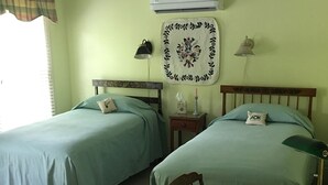 Una camera con due letti singoli, una scrivania con sedia, un condizionatore d'aria a parete e un elemento decorativo a parete.