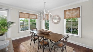Ein Esszimmer mit Holztisch, sechs Stühlen, einer Kronleuchter und großen Fenstern mit Jalousien.