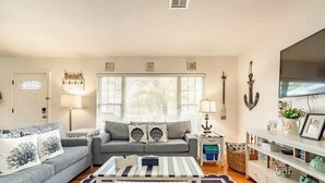 A living room with a sofa, a coffee table, a TV, and a bookshelf. - Backyard Oasis, Htd Pool/Hot Tub, Beaches, No Fees (Sarasota)