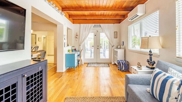 A spacious living room with a wooden ceiling, a grey sofa, and a television on a black cabinet. - Backyard Oasis, Htd Pool/Hot Tub, Beaches, No Fees (Sarasota)