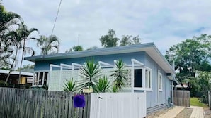 Une maison de plain-pied à la façade bleu clair, avec une clôture blanche et une allée pavée.