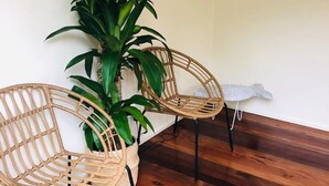 Deux fauteuils en osier, séparés par un pot de fleurs, un plancher en bois et un mur blanc.