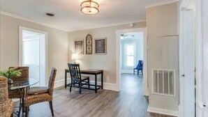 A dining area with a round table and wicker chairs, a chandelier, and framed artwork on the wall.