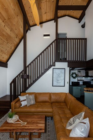 Een ruime woonkamer met een bruine leren bank, een houten salontafel en een trap met donkere houten leuningen.
