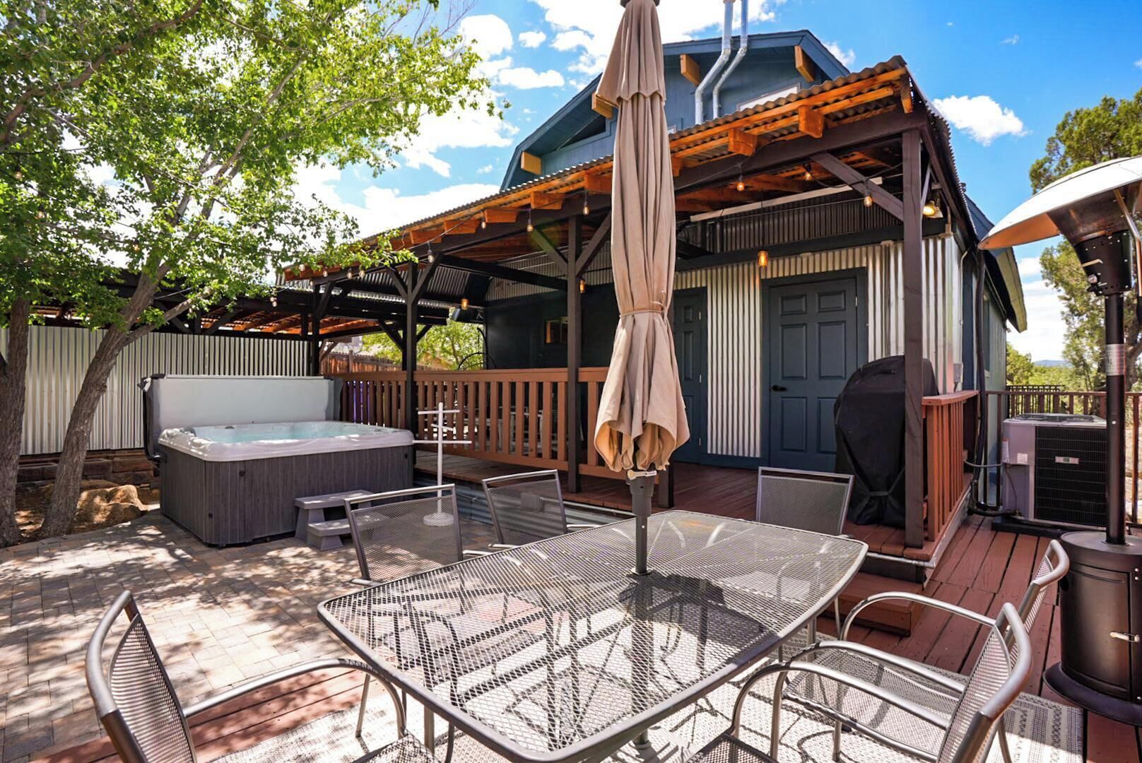 A covered outdoor deck with a hot tub, seating area, and a pergola with umbrellas.