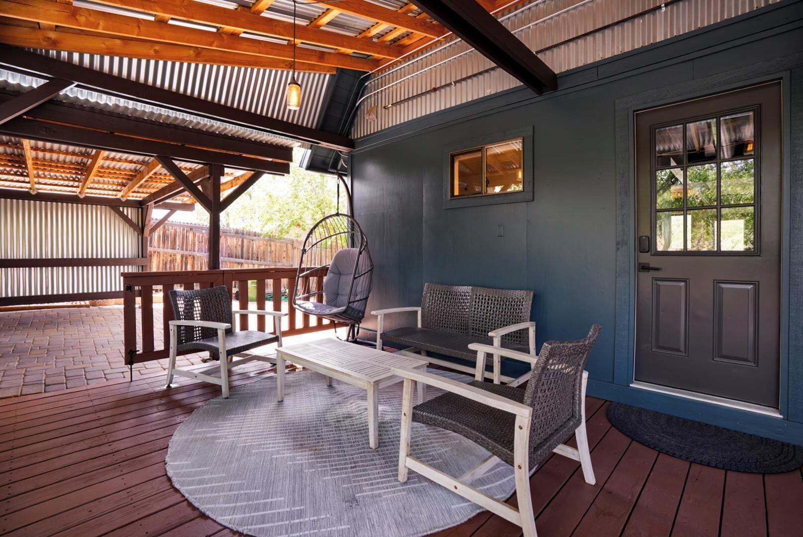 Un patio cubierto con mobiliario exterior, una silla colgante y una puerta con ventanal.