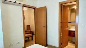Un dormitorio con cama, una puerta de madera, una silla y un baño visible a través de una puerta abierta.