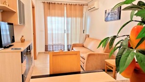 Una sala de estar con sofá, televisor, mesa de centro y planta.