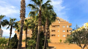 Un edificio de varios pisos con balcones, rodeado de palmeras y un jardín ajardinado.