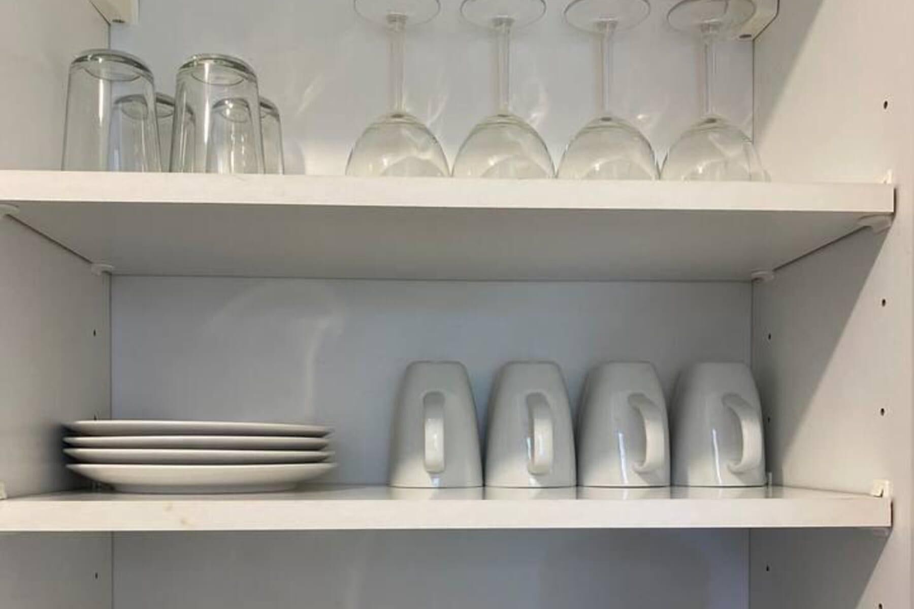 A white shelf with wine glasses and plates.