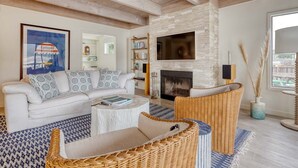 A living room with a white sofa, a fireplace, a bookshelf, and a large window. - Bolinas Beach Home - Over the water with spectacular views (Bolinas)