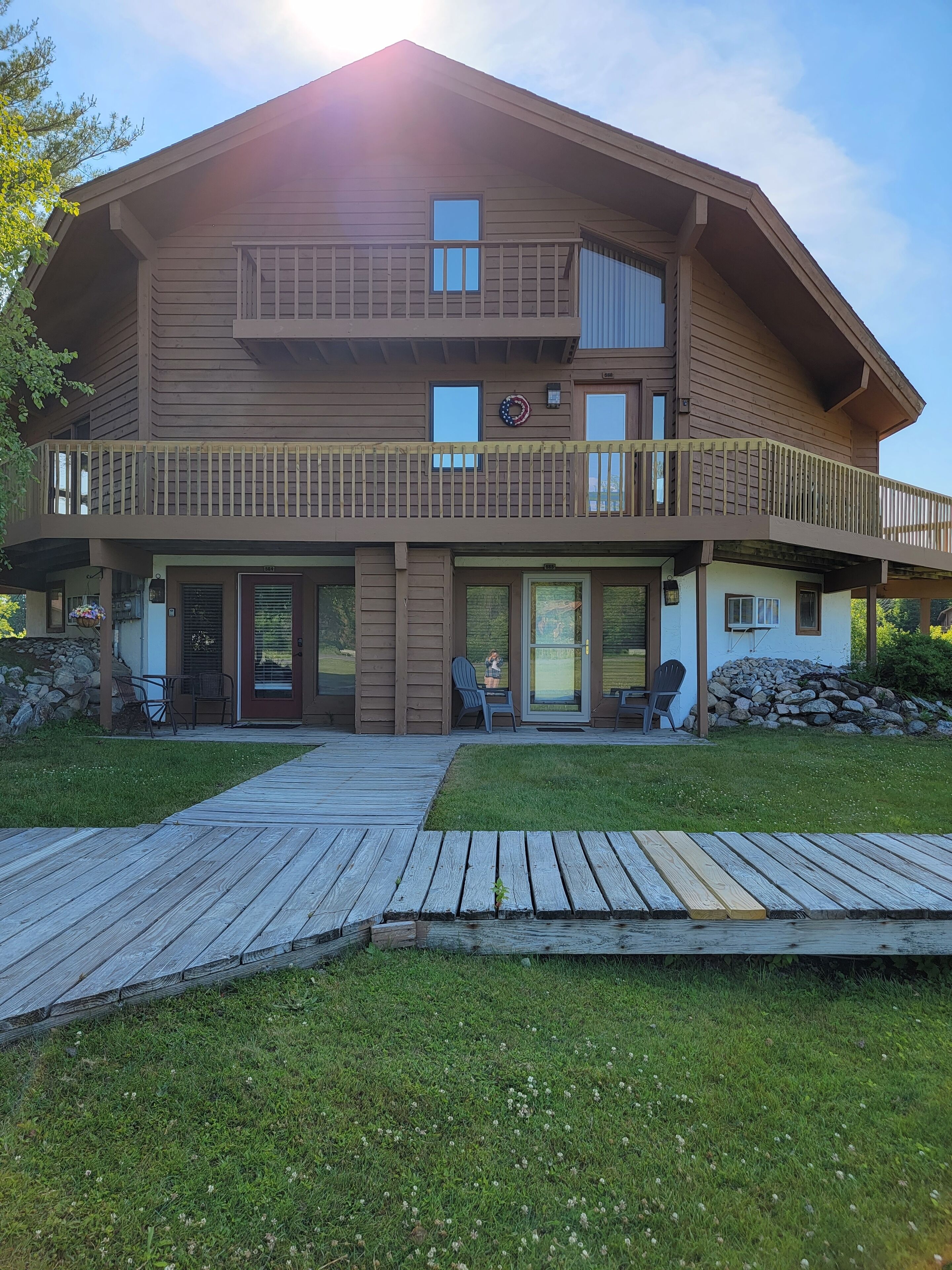 Une maison à deux étages, avec une façade en bois, un balcon et une véranda à l’avant, équipée de chaises.