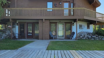 Une maison à deux étages, avec une façade en bois, un balcon et une véranda à l’avant, équipée de chaises.