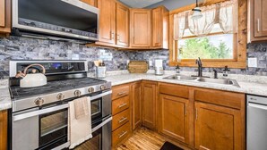 A kitchen with wooden cabinets, a stainless steel range, a built-in oven, a dishwasher, and a window with curtains. - Farmhouse Retreat*Great View*Hot Tub*Wineries (Traverse City)