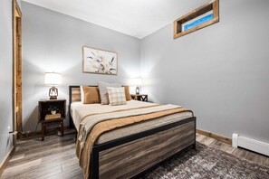 A bedroom with a bed, two bedside tables, a nightstand, a wall-mounted picture, and a radiator. - Farmhouse Retreat*Great View*Hot Tub*Wineries (Traverse City)