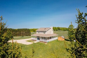 A two-story house with a large porch and a small shed, surrounded by a grassy yard and trees. - Farmhouse Retreat*Great View*Hot Tub*Wineries (Traverse City)