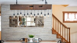 A dining area with a wooden table, chairs, and a rustic wall with hanging light fixtures. - Farmhouse Retreat*Great View*Hot Tub*Wineries (Traverse City)