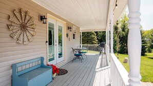 A covered porch with a bench, a table with chairs, and a decorative wall piece. - Farmhouse Retreat*Great View*Hot Tub*Wineries (Traverse City)