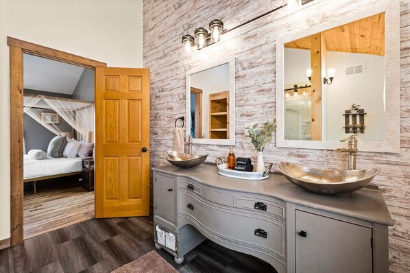 A bathroom with a vanity, two sinks, a mirror, and a wooden door.