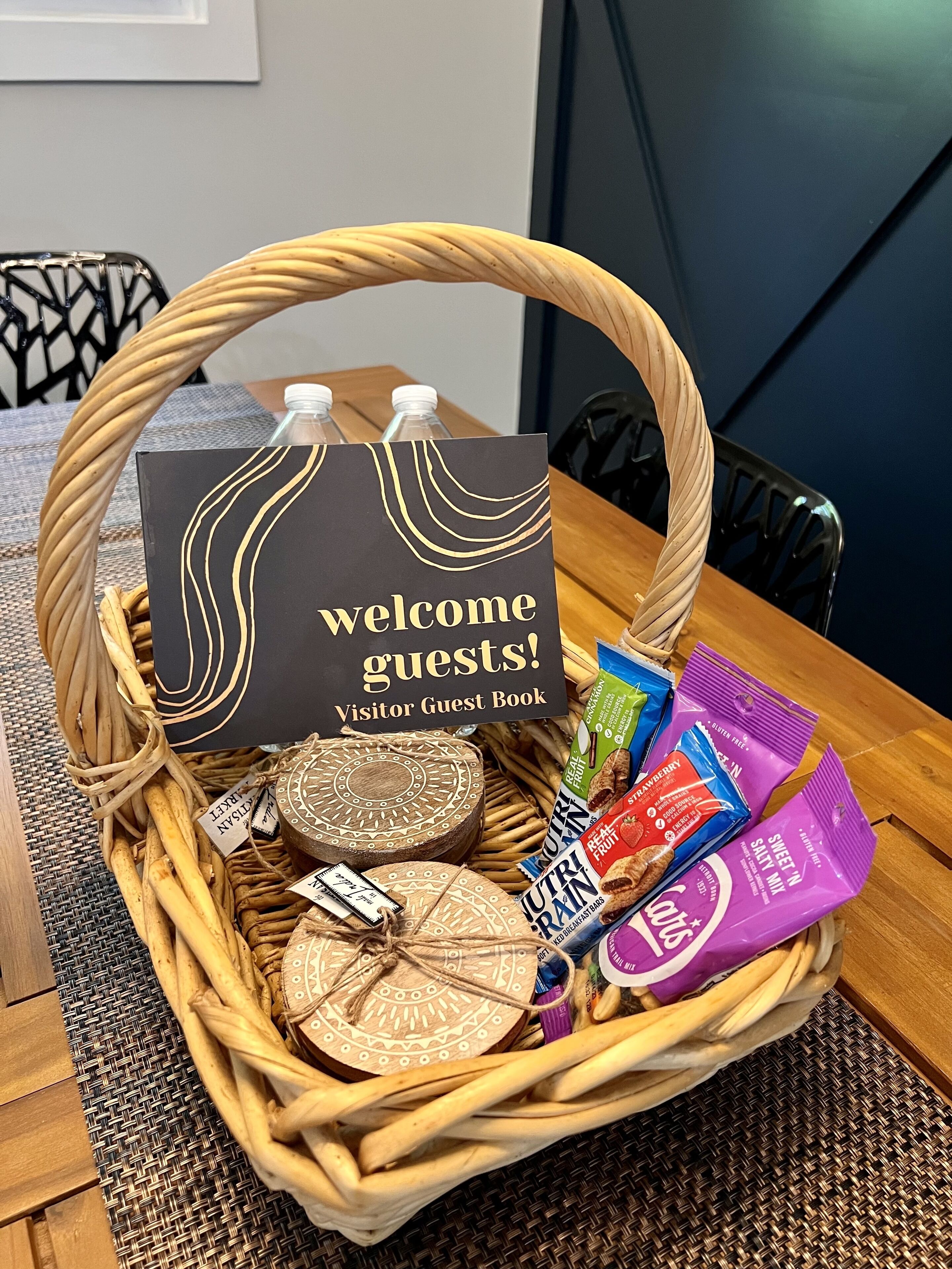 Un panier en osier avec une pancarte indiquant « Bienvenue à nos invités ! », un livre d’or pour les visiteurs et un assortiment de collations.