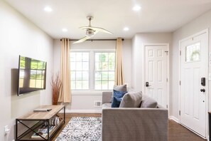 Un soggiorno moderno con un divano grigio, un tavolino in legno, una TV a schermo piatto montata a parete e una ventola a soffitto.