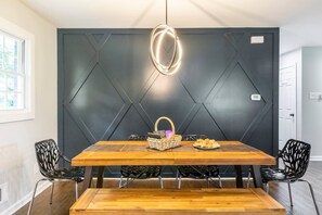 Un'area pranzo con un tavolo in legno, sedie nere, un cesto di vimini e un piatto di pasticcini.