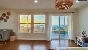 Un salon spacieux doté d’une grande porte-fenêtre coulissante donnant sur un balcon, d’un plancher en bois et d’un luminaire au plafond.