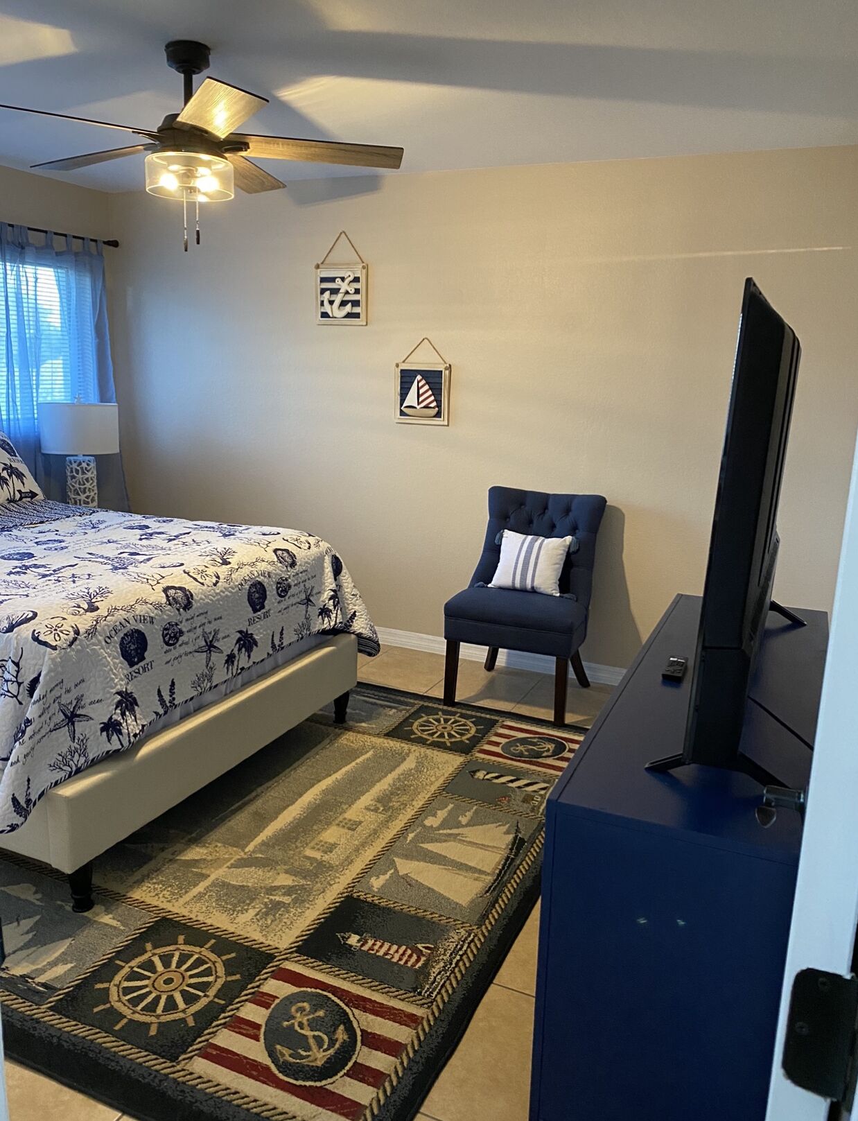 Une chambre à coucher comprenant un lit, une chaise, un bureau, un téléviseur, un ventilateur de plafond et un tapis.