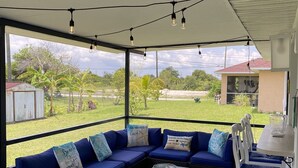 A covered outdoor seating area with a blue sofa set, a wicker coffee table, and a view of the surrounding landscape. - Cozy, Clean, Convenient With A Beach Feel (Cape Coral)