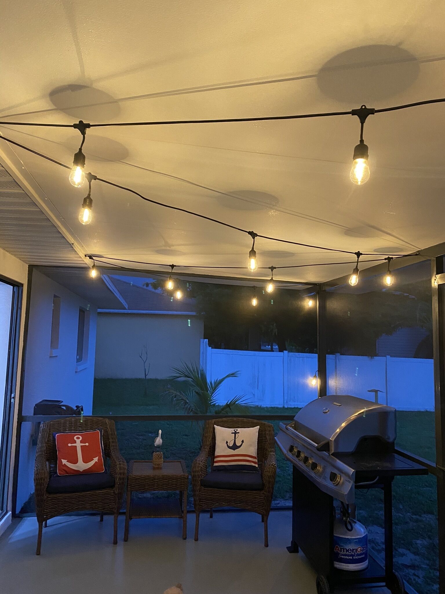 An outdoor patio with wicker chairs, a grill, and string lights.