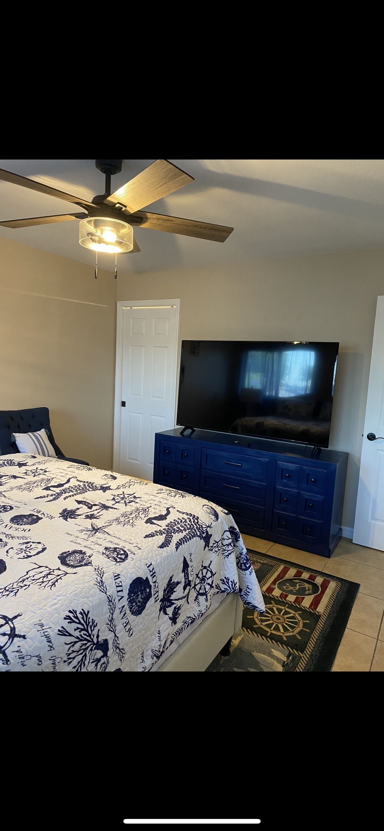 A bedroom with a bed, a TV, a ceiling fan, and a dresser.