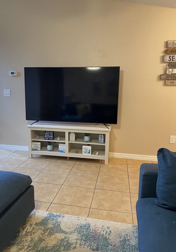 A living room with a flat-screen TV on a wooden stand, a dark-colored sofa, and a patterned rug. - Cozy, Clean, Convenient With A Beach Feel (Cape Coral)