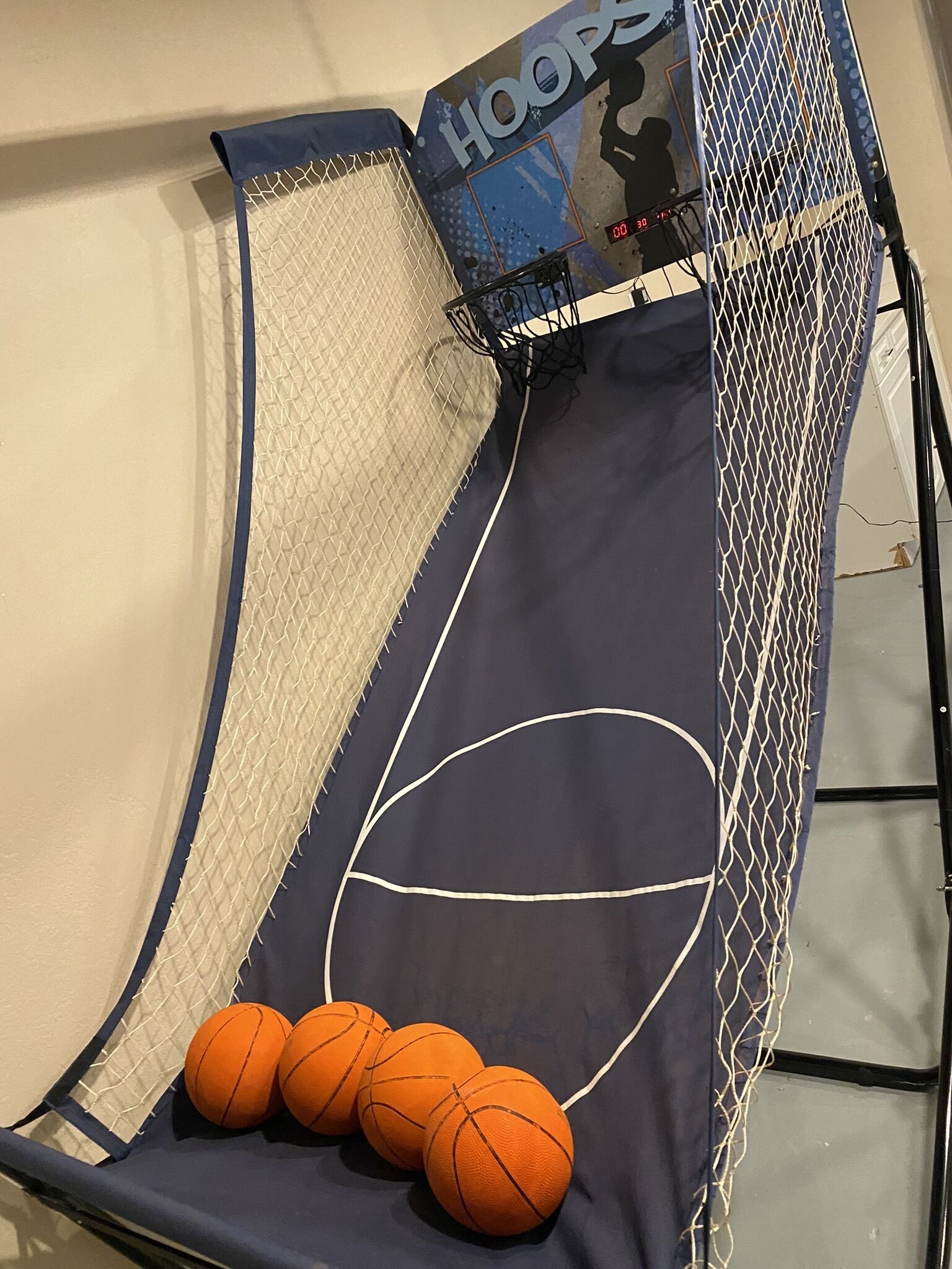 A basketball hoop with a net and three basketballs placed on a blue surface with a basketball court design.