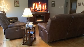 A living room with two brown leather sofas, a wooden coffee table with a lamp, a fireplace, and a television displaying a fire scene. - The Farmhouse- country charm, room for family visiting, relaxing, or gathering  (West Union)