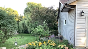 A residential garden with a lawn, various plants, and a house with siding and a lantern. - The Farmhouse- country charm, room for family visiting, relaxing, or gathering  (West Union)
