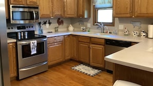 A kitchen with wooden cabinets, stainless steel appliances, a window with a curtain, and various kitchen decor. - The Farmhouse- country charm, room for family visiting, relaxing, or gathering  (West Union)