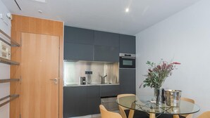 Une cuisine compacte dotée d’appareils électroménagers modernes, un coin repas avec une table en verre et des chaises en bois, et une petite plante décorative.