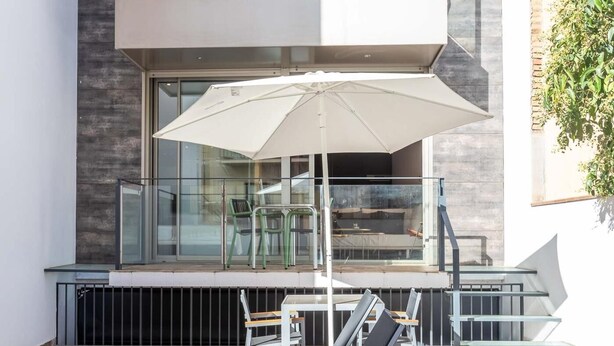 Un espace extérieur moderne, aménagé avec une balustrade en verre, un parasol blanc et des fauteuils de relaxation.