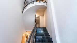 Un escalier en colimaçon avec des marches noires et une rampe en métal, menant à un palier doté d’une porte.