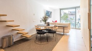 A modern living room with a dining area, a sofa, a TV, and a staircase. - My Space Barcelona apartment with large terrace close to Barraquer clinic (Barcelona)