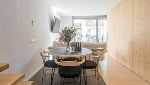 A modern living room with a round dining table, black chairs, a beige sofa, and a wooden accent wall. - My Space Barcelona apartment with large terrace close to Barraquer clinic (Barcelona)