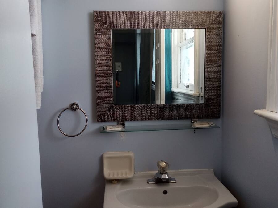 A bathroom with a sink, mirror, towel rack, and a glass shelf with toiletries.