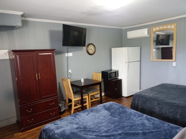 A room with two beds, a wooden cabinet, a television, a clock, a microwave, and a refrigerator.