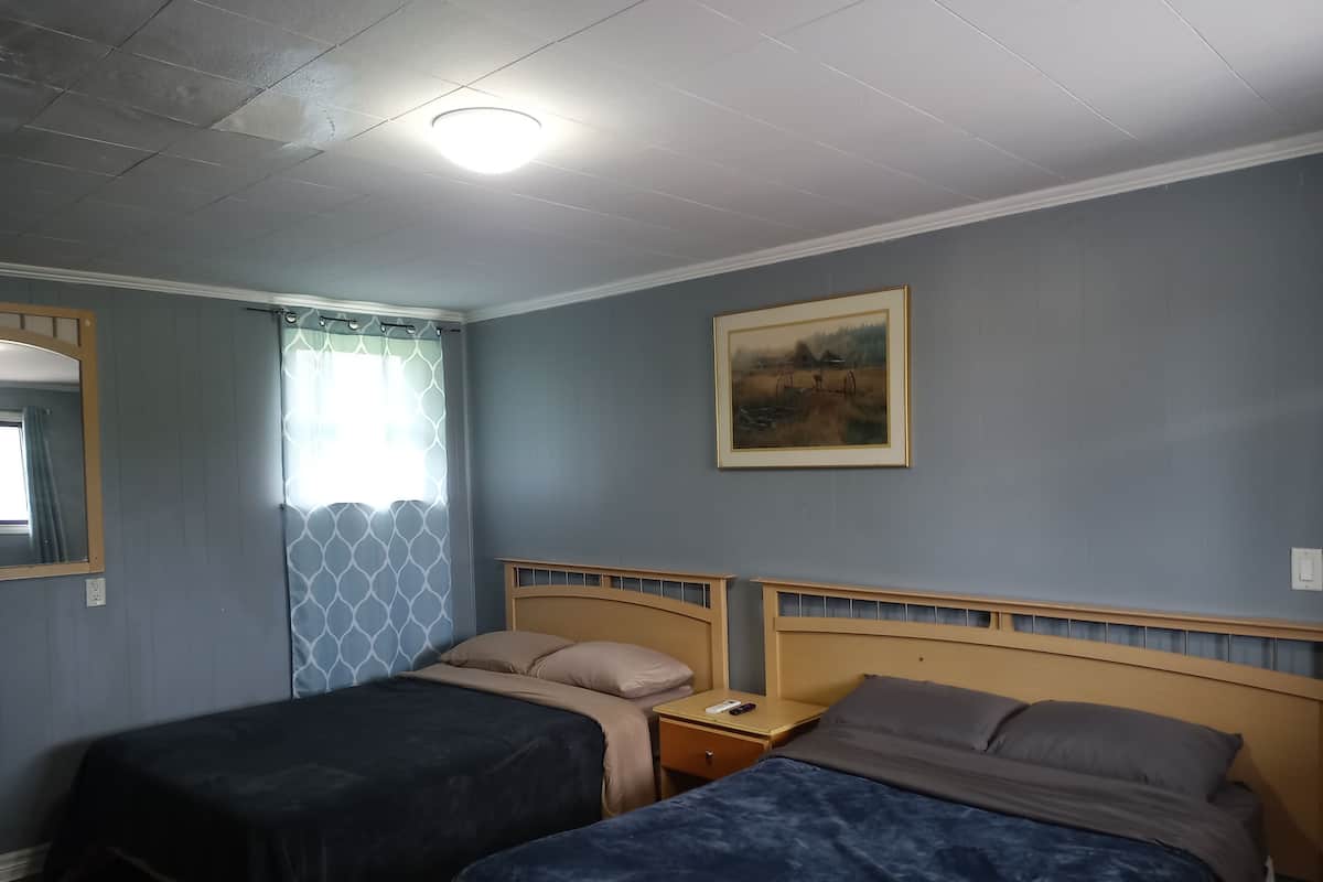 Un dormitorio con dos camas individuales, una mesita de noche, un espejo, una ventana con cortinas y un cuadro en la pared.