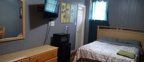 Un dormitorio con cama, cómoda, televisor y obra de arte en la pared.