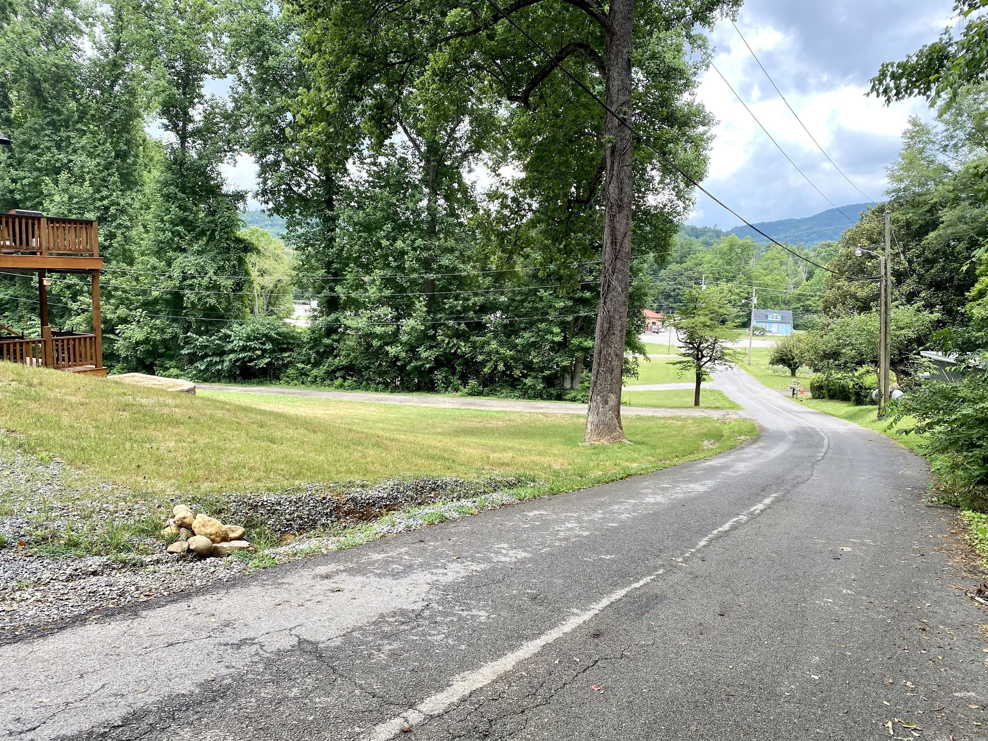 A rural road with a wooden structure on the left, surrounded by greenery and trees.