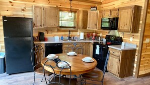 A wooden cabin-style kitchen with a black refrigerator, wooden cabinets, a dining table with chairs, and a microwave. - Black Bear Retreat • 2Bed 2Bath Cabin • Peaceful Retreat (Townsend)