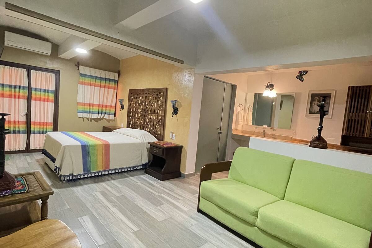 A room with a bed, a green sofa, a wooden table, and a small table with a chair.