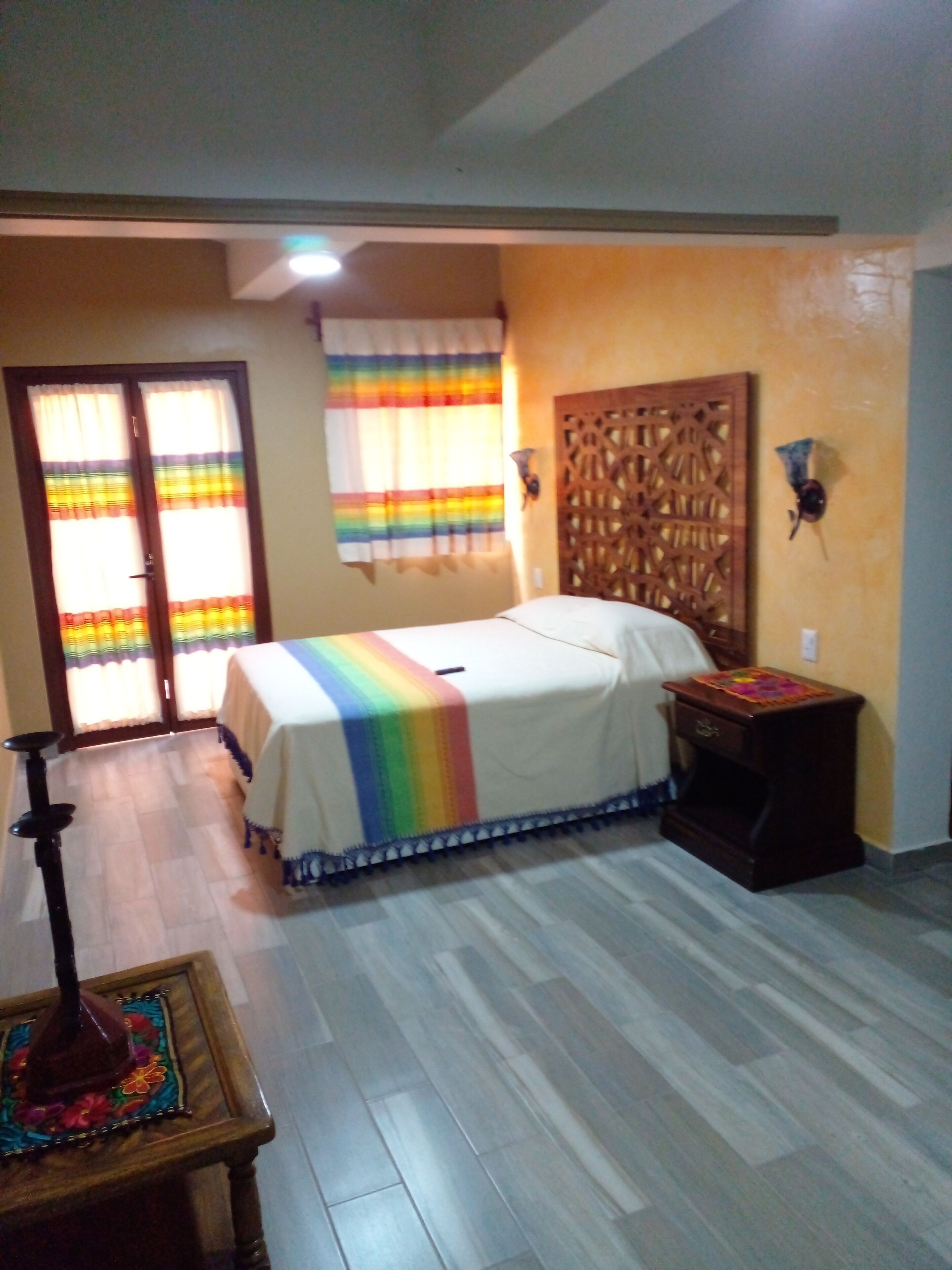 A bedroom with a bed, a wooden headboard, a nightstand, a table with a decorative item, and a door with curtains.