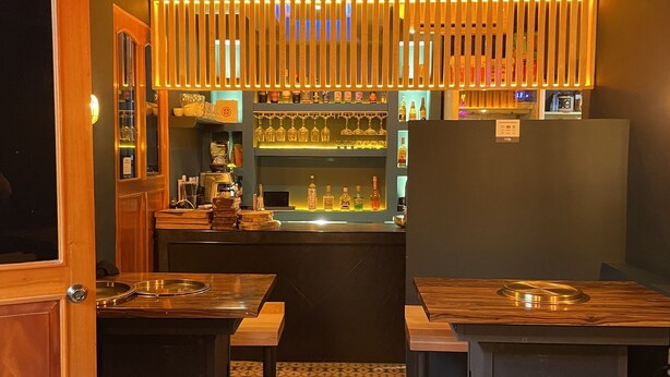Un espace bar avec des tables et des bancs en bois, un sol à motifs et une étagère remplie de bouteilles et de verres.